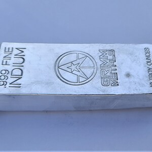 May include: A silver indium bar with the text ".999 FINE INDIUM" and "GRIMM METALS" stamped on the surface. The bar weighs 283.5 grams. The bar has a shiny, reflective surface.