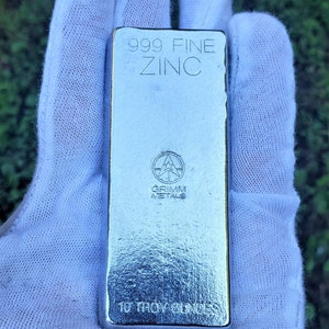 May include: A silver bar of 999 fine zinc, weighing 10 troy ounces. The bar is stamped with the words "999 FINE ZINC" and "GRIMM METALS".