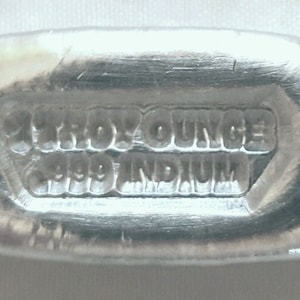 May include: A silver bar with the inscription "1 Troy Ounce .999 Indium" on the front.