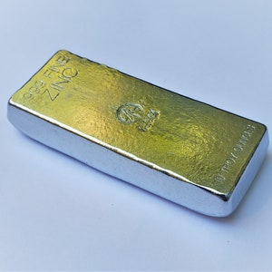 May include: A silver bar of 99.9 fine zinc, weighing 10 troy ounces. The bar has a textured surface and is marked with the words "999 FINE ZINC" and "10 TROY OUNCES".