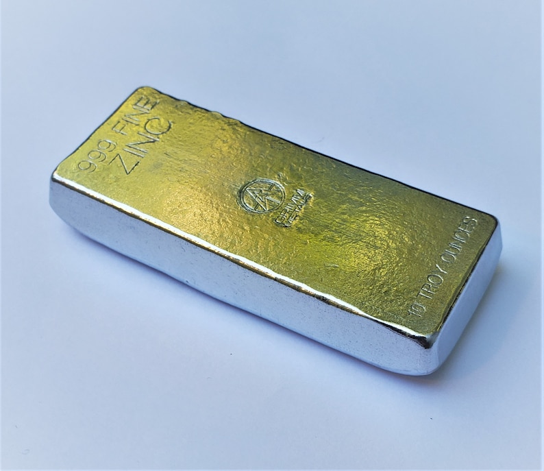 May include: A silver bar of 99.9 fine zinc, weighing 10 troy ounces. The bar has a textured surface and is marked with the words "999 FINE ZINC" and "10 TROY OUNCES".