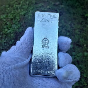 May include: A silver bar of 999 fine zinc, weighing 10 troy ounces. The bar is stamped with the Grimm Metals logo and the words "999 Fine Zinc" and "10 Troy Ounces".