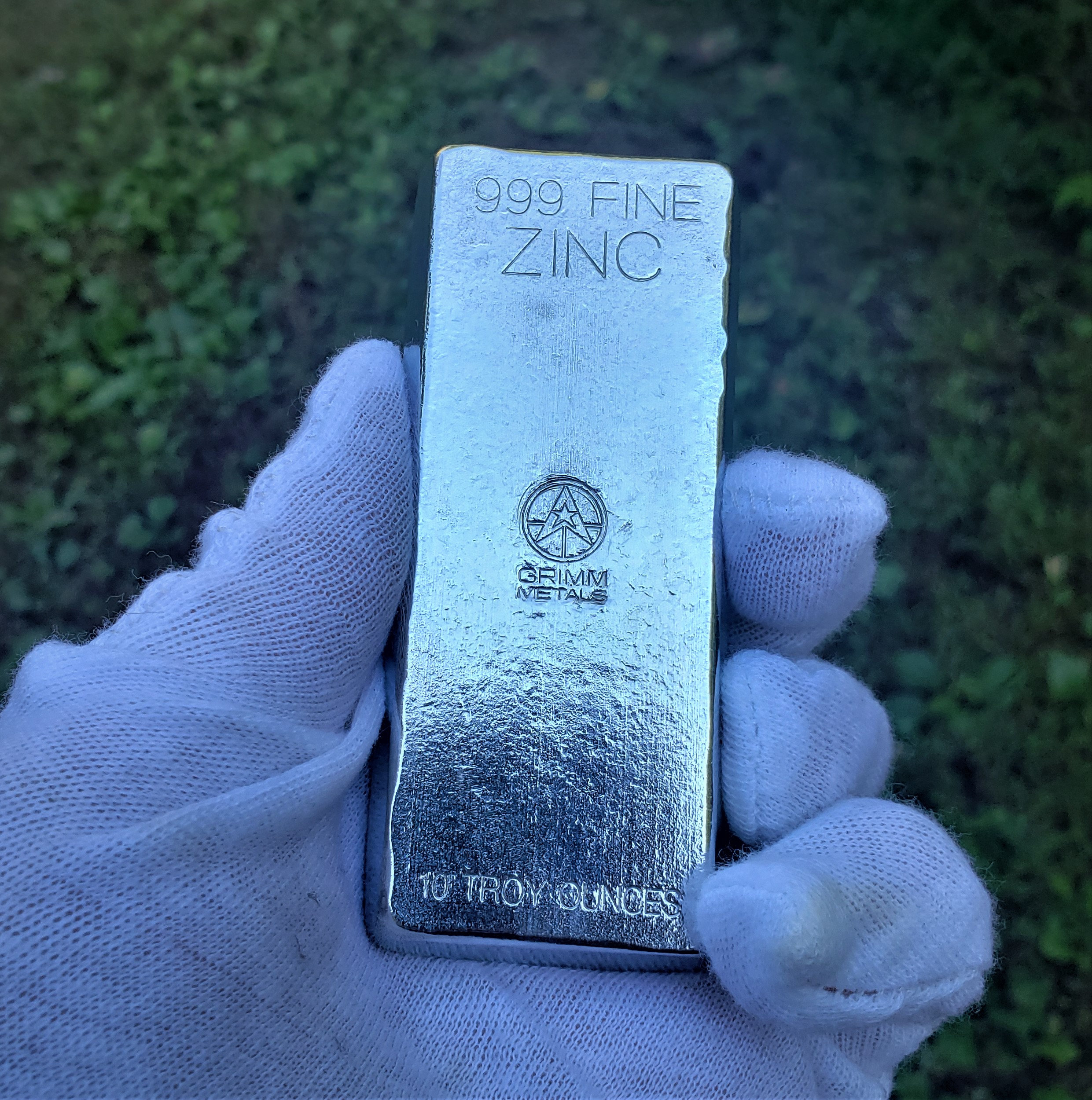 May include: A silver bar of 999 fine zinc, weighing 10 troy ounces. The bar is stamped with the Grimm Metals logo and the words "999 Fine Zinc" and "10 Troy Ounces".