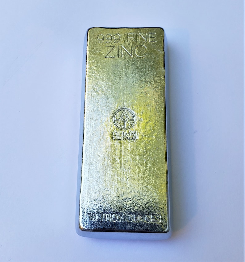 May include: A silver bar of 999 fine zinc, weighing 10 troy ounces. The bar is stamped with the Grimm Metale logo and the words "999 Fine Zinc" and "10 Troy Ounces".