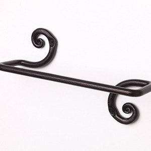 May include: Black metal towel rack with decorative scrollwork on the ends. The rack is mounted to a white wall.