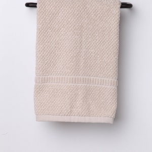 May include: A beige hand towel hangs on a black metal towel rack with a decorative scroll design.