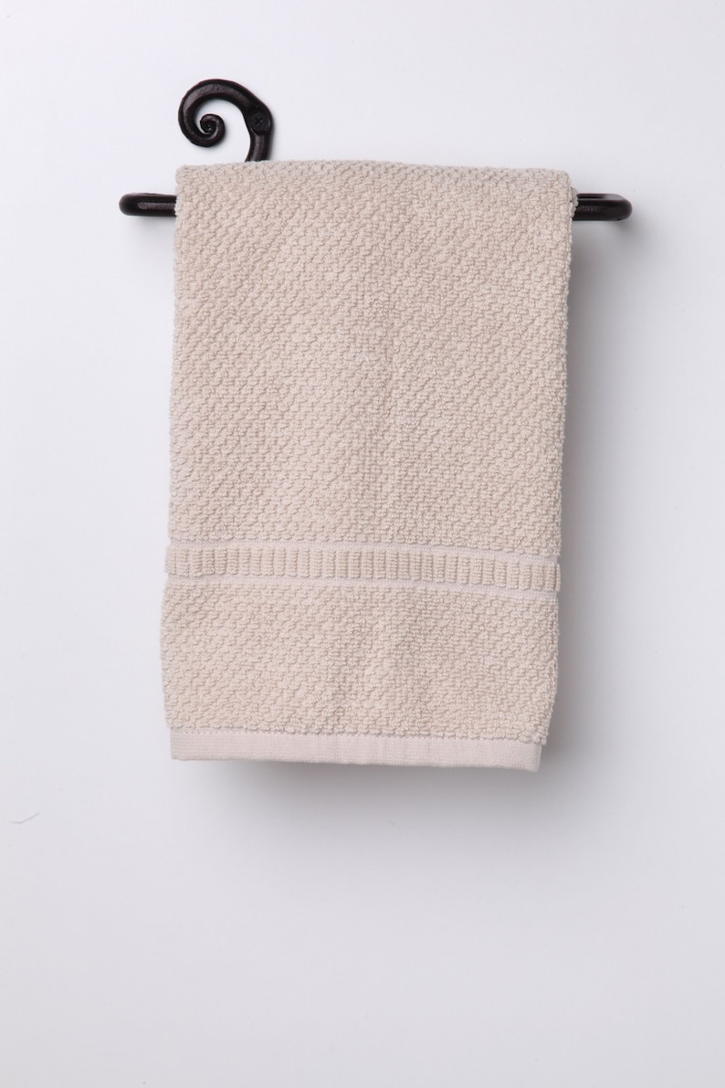 May include: A beige hand towel hangs on a black metal towel rack with a decorative scroll design.