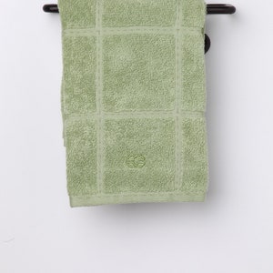 May include: A green towel with a decorative pattern hangs on a black metal towel rack with a scroll design.