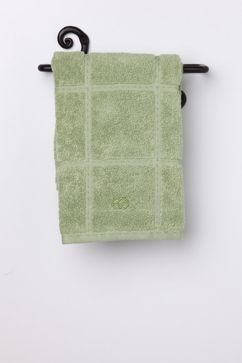 May include: A green towel with a decorative pattern hangs on a black metal towel rack with a scroll design.