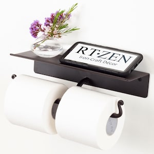 May include: Black metal double toilet paper holder with a shelf and a phone holder. The shelf has a small vase with purple flowers. The text on the phone holder reads "RT:ZEN Iron-Craft Décor".