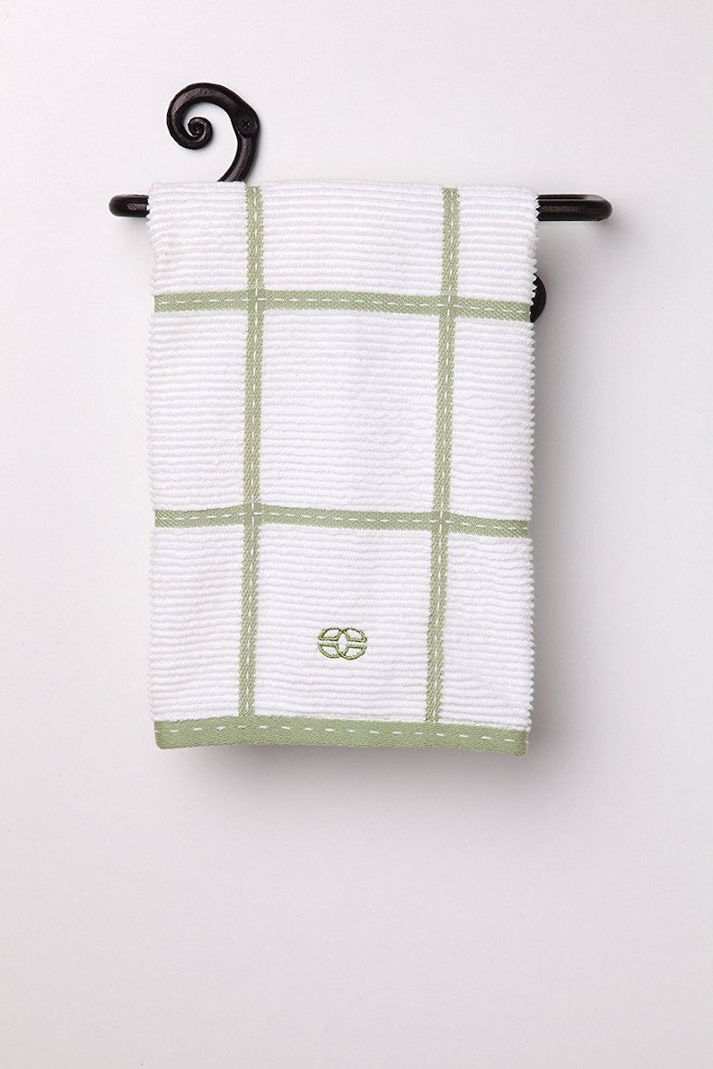 May include: A white kitchen towel with green checkered pattern and a green embroidered logo hangs on a black metal towel rack with a decorative scroll.