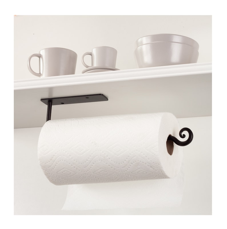 Pode incluir: Suporte de papel toalha de metal preto montado sob uma prateleira branca. Um rolo de papel toalha branco est&aacute; no suporte. O suporte tem um design decorativo de rolagem.