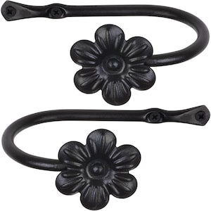 May include: Two black metal curtain tiebacks with a flower design. Each tieback is shaped like a loop with a flower at the end.