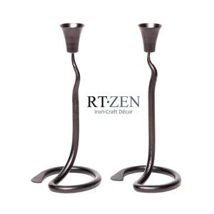 May include: A pair of black metal candle holders with a unique, curved design. The holders are made of iron and have a matte finish. RT.ZEN Iron-Craft Décor.