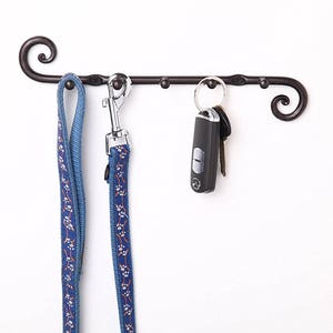 May include: A black metal wall-mounted hook with two blue leashes and a set of keys hanging from it.
