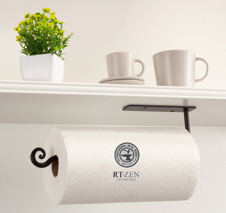 Pode incluir: Suporte de papel toalha de metal preto montado sob uma prateleira branca. O suporte tem um design de rolagem decorativo e um logotipo redondo que diz "Professional Metal Works RT-ZEN Iron-Craft Decor".
