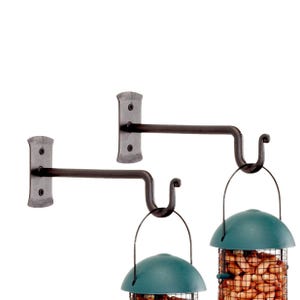 May include: Two black metal bird feeder hooks mounted on a wall. Each hook has a curved arm and a U-shaped hook at the end. Two bird feeders are hanging from the hooks, filled with peanuts.