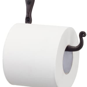 May include: A black wrought iron toilet roll holder with a decorative scroll design. The holder is mounted to a wall and has a roll of white toilet paper on it.