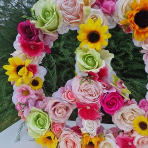 May include: A peace sign made of artificial flowers. The flowers are in shades of pink, white, yellow, and green. The peace sign is a popular symbol of peace and love.