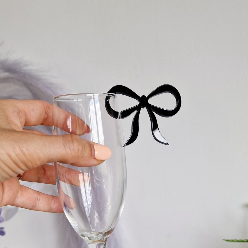 Peut inclure: Un charme en forme de n&oelig;ud noir en plastique pour une fl&ucirc;te &agrave; champagne ou un verre &agrave; vin.
