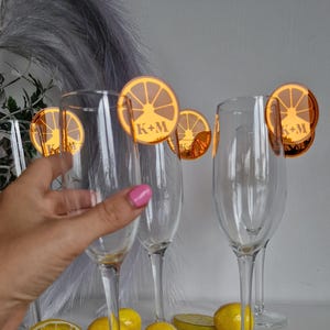 May include: Four champagne flutes with orange lemon slice shaped place cards with the initials K+M printed on them.