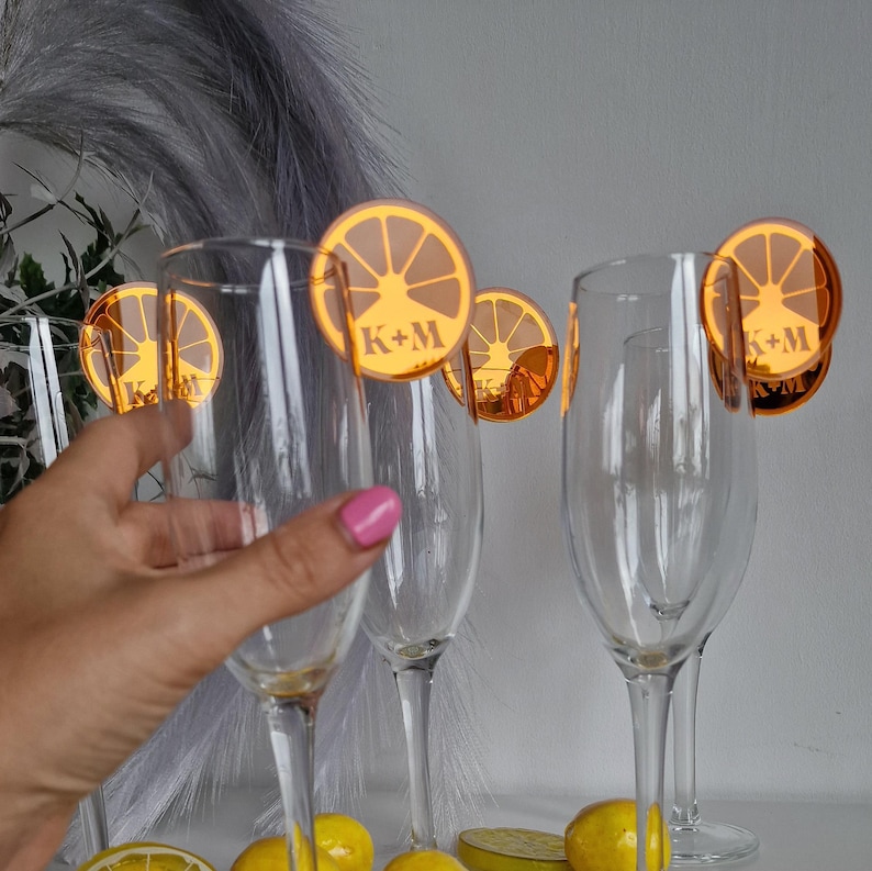 May include: Four champagne flutes with orange lemon slice shaped place cards with the initials K+M printed on them.