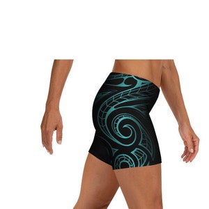 May include: Black athletic shorts with a teal tribal design. The shorts are form-fitting and feature a repeating pattern of swirls and lines on the sides. The shorts are designed for athletic activities.