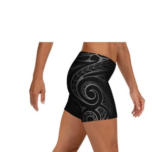 May include: Black athletic shorts with a gray tribal design on the side. The shorts are form-fitting and appear to be made of a stretchy material. The shorts are shown on a person.