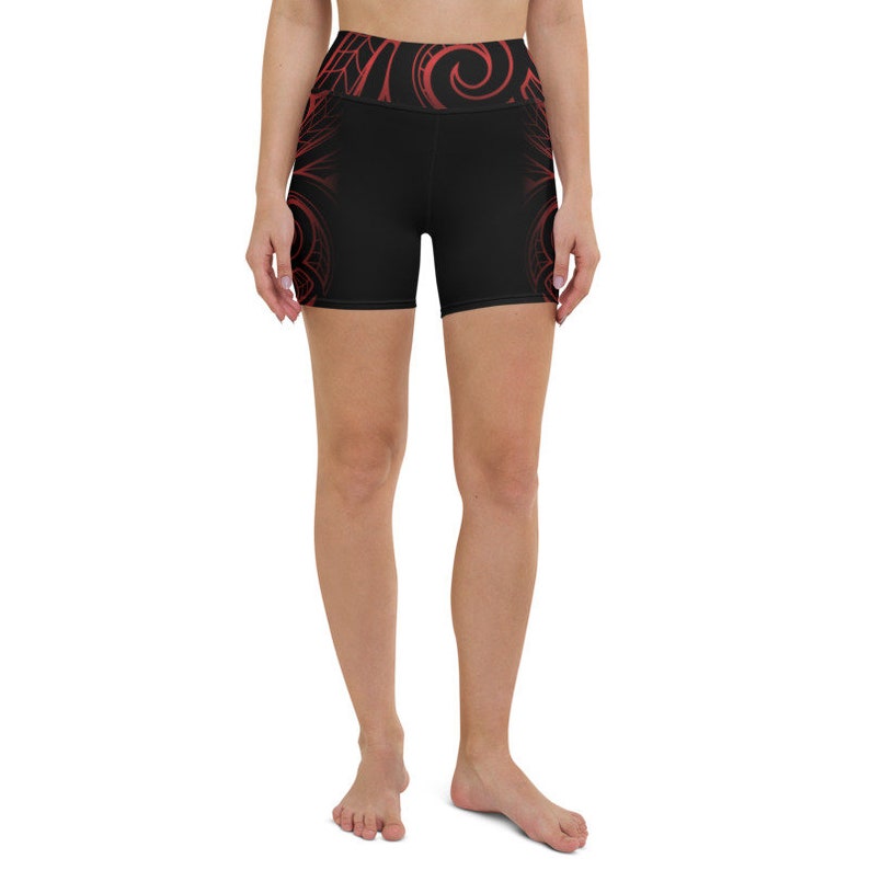 May include: Black yoga shorts with a high waistband and red tribal-inspired designs. The shorts feature a repeating pattern on the waistband and along the sides, creating a visually striking athletic garment.