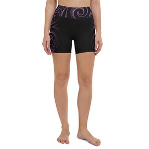 May include: Black yoga shorts with a high waistband and a purple tribal design. The shorts feature a repeating pattern on the sides and waistband. The shorts are made of a stretchy material.