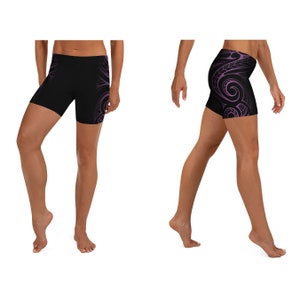 May include: Black athletic shorts with a purple tribal design. The shorts are form-fitting and feature a swirling pattern on the side. The shorts are designed for athletic activities and are made of a stretchy material.