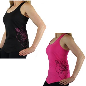 Op de afbeelding: Zwarte en roze tanktops met een groot hibiscusbloemdesign aan de zijkant. De tanktops hebben een ronde hals en een racerback-stijl. De hibiscusbloem is omlijnd in een contrasterende kleur.