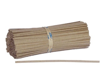 Pode incluir: Um feixe de palitos de madeira finos, castanhos claros, presos por um elástico bege com texto azul. Um palito está separado do feixe. Os palitos têm aproximadamente 25 cm de comprimento.