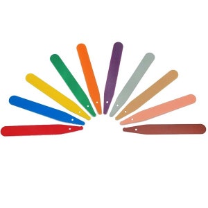 May include: Eleven colourful plant labels arranged in a semi-circle. The labels are in various colours, including red, blue, yellow, green, orange, purple, grey, tan, pink, and brown. Each label has a small hole near the top.