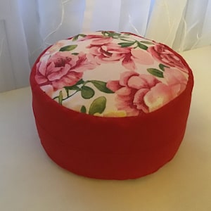 Puede incluir: Un cojín redondo rojo y blanco con flores y una base de tela roja.