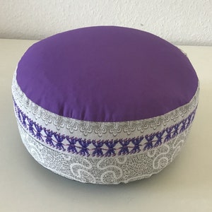 Puede incluir: Cojín de meditación morado con un borde bordado blanco y morado.