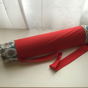 Puede incluir: Portador de tapete de yoga rojo con un patrón floral blanco y azul. El portador tiene una correa roja larga.