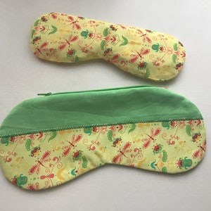 Puede incluir: Dos antifaces. Uno tiene forma larga y curva, y el otro es de tamaño más pequeño a juego. Ambos son amarillos con un estampado de libélulas y flores. La máscara más grande tiene la parte superior verde y una cremallera.