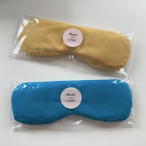 May include: Two eye masks, one yellow and one blue, are packaged in clear plastic bags. Both masks have a white circle with the text "Made with LOVE" printed on them.