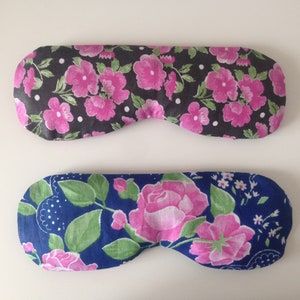 May include: Two floral eye masks. One is black with pink flowers and white polka dots. The other is blue with pink roses and green leaves.