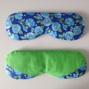 Puede incluir: Dos antifaces. El antifaz superior tiene un estampado floral azul sobre un fondo azul oscuro. El antifaz inferior es verde con un estampado floral azul en los bordes. Ambos antifaces son de tela y están diseñados para cubrir los ojos.