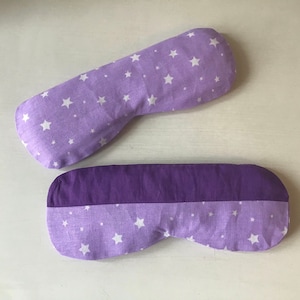May include: Two purple eye masks with white stars. One mask is solid purple, the other has a white star pattern.
