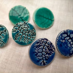 May include: Five ceramic round buttons with a white background and a blue, green, or teal crackle glaze pattern.