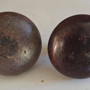 May include: Two antique, round wooden knobs. One knob is a dark brown with a copper-colored patina, and the other is a deep reddish-brown with visible wood grain. These knobs are likely for furniture.