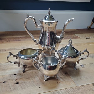 May include: A set of four silver-plated tea or coffee service pieces, including a teapot, creamer, sugar bowl, and a small cup. The pieces are all decorated with ornate designs and have a polished finish.