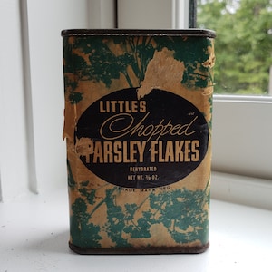 May include: A vintage metal tin of Little's Chopped Parsley Flakes. The tin is green and brown with a black oval label that reads "Little's Chopped Parsley Flakes" with the text "Dehydrated Net Wt. 3/8 oz. Trade Mark Reg."