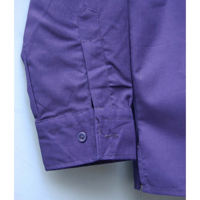 May include: A long-sleeved, purple button-down shirt with a single button cuff. The shirt has a plain design and is made of a smooth, woven fabric.