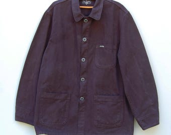 May include: A dark purple work jacket with a button-up front, two front pockets, and a collar. The jacket is hanging on a wooden hanger. The brand name "Cap Field" is visible on the hanger.