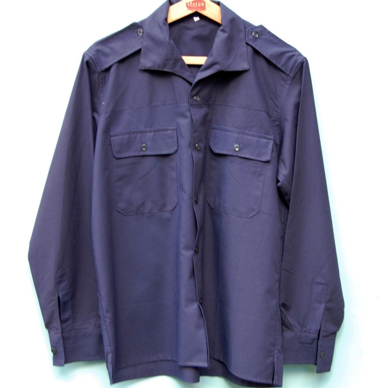 May include: A dark blue long-sleeved shirt with two flap pockets and a button-up front.