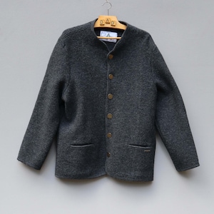 Puede incluir: Una chaqueta de color gris oscuro con mangas largas, cuello alzado y cierre frontal de botones. La prenda presenta dos bolsillos ribeteados en la parte inferior y un tejido texturizado similar al fieltro. Una etiqueta blanca es visible.